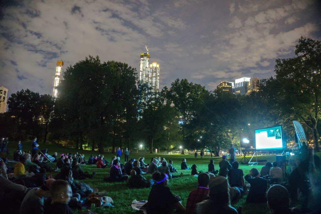 people watch a screen sitting in the grass